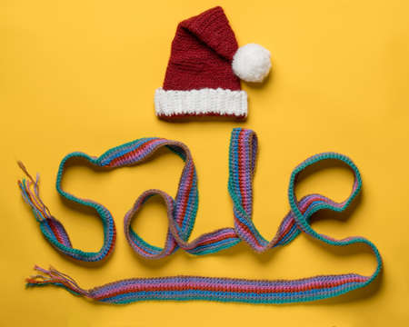 Inscription sale from a scarf and a hat of Santa Claus on top, on a yellow background. Concept of New Years discounts and shopping.の写真素材