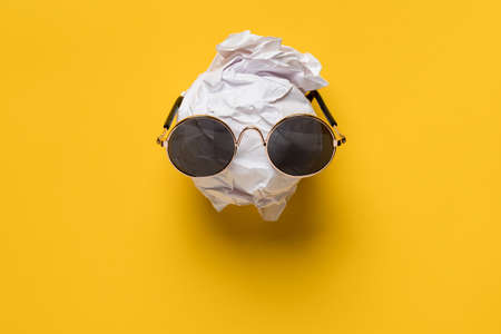 Crumpled white paper and sunglasses on it look like a face against a yellow background. Creative idea. Top view.の写真素材