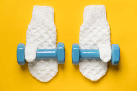 Two dumbbells on white knitted mittens on a yellow background. Healthy and active lifestyle concept. Top view.の写真素材