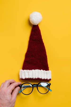 Red and white knitted hat of Santa Claus and the glasses under it, which are straightened by the hand, looks like a face.の写真素材