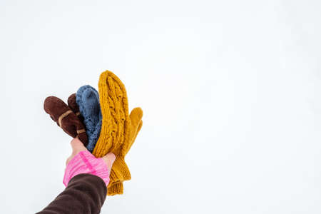 Hand holds several pairs of knitted warm mittens of different colors, against a background of white snow. Copy space.の写真素材