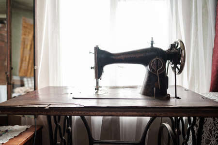 Vintage mechanical sewing machine with a table stands by a window in a rustic house.の写真素材