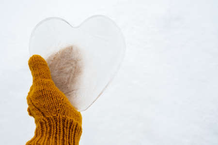 Hearts - a symbol of love, made of ice, are held by a hand in warm yellow knitted mittens. Valentines Day. Romantic concept. Copy space.の写真素材