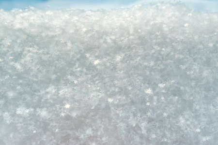 Snowflakes glow in the sun, on fluffy snow, on a frosty winter day. Copy space. Abstract background.
