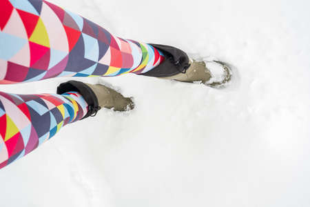 Slender female legs in bright multicolored leggings and warm waterproof boots stand in a deep snowdrift on a frosty winter day. Lifestyle.の写真素材