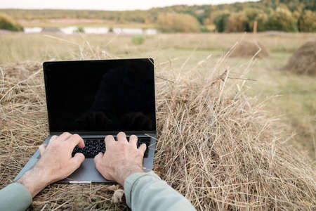 Remote work with a laptop on a haystack, against the backdrop of a beautiful rural landscape, on a summer evening. Lifestyle.の写真素材