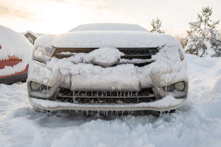 Car is covered with snow and ice, icicles hang from the bumper of the auto, against the sky, on a frosty winter evening.の写真素材