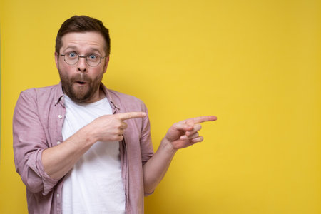 Surprised man in glasses points to something with his index finger and looks at the camera. Copy space.の写真素材