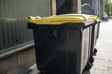 Plastic garbage containers stand near the buildings showcase, on a city street, on a spring day.の写真素材