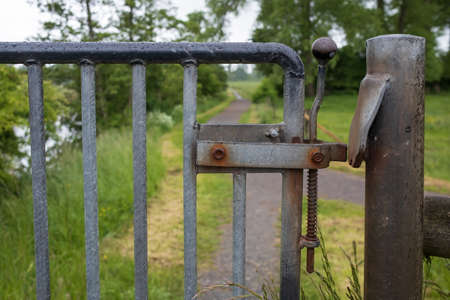 Metal gate with a latch, limiting the passage to the fenced area, outdoors.の写真素材