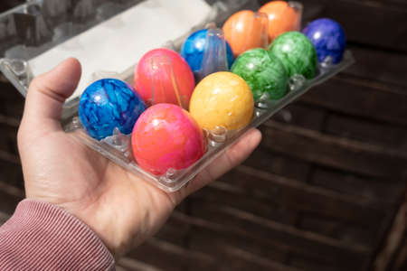 Male hand holds a transparent tray with bright colored Easter eggs, against the background of a black table.の写真素材