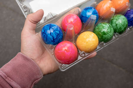 Male hand holds a transparent tray with bright colored Easter eggs, against the background of a black table.の写真素材