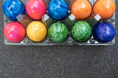 Bright colored Easter eggs in a transparent tray, on a black table. Copy space. Top view.の写真素材