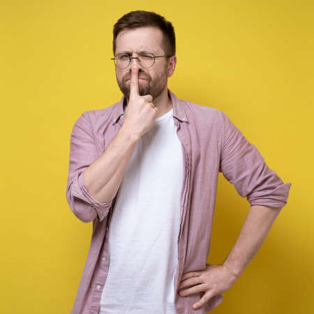Young attractive man in glasses thought about something, he put finger to his nose and screwed up one eye. Yellow background.の写真素材