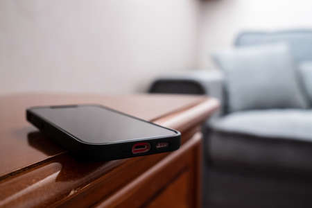 Smartphone is inadvertently left on the edge of a wooden table and may fall. Concept of careless attitude to things.の写真素材