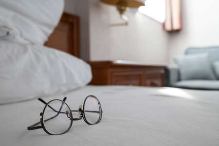 Glasses lie on the bed, against the backdrop of a cozy home interior.