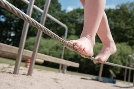 Kid tightrope walker balances with bare feet on a cordの写真素材