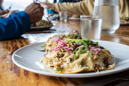 Food in a plate on a wooden table, next to a glass cup with cold water and a decanter, people are eating in the background.の写真素材