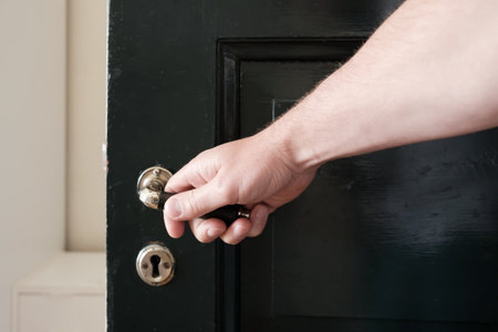 Male hand wants to close a black wooden door, holding on to a metal handle, against the background of a white wall.の写真素材