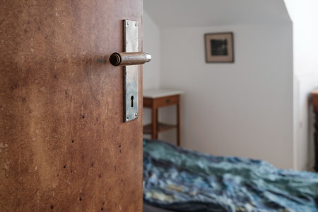 Open wooden door, against the background of a bed and a room with white walls, with natural light from the window.の写真素材