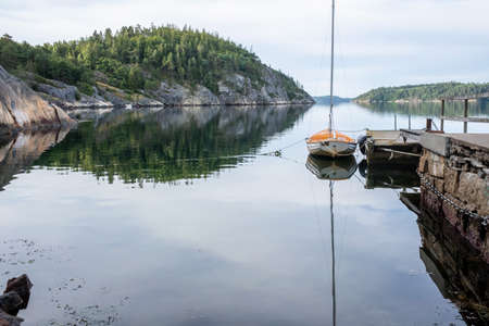 Sailboat moored to the pier, against the backdrop of a rocky shore and sky. Beautiful seascape.