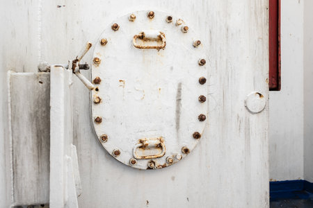 Details of a white iron door on the ship, with rivets and rust, and a twist lock.の写真素材