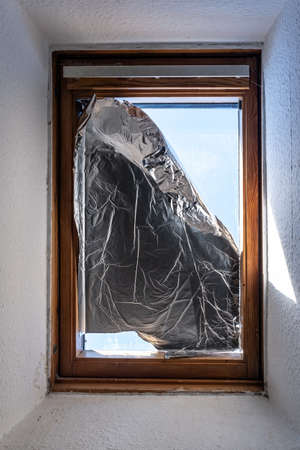 Window covered with foil to prevent sunlight from entering house during heatの写真素材