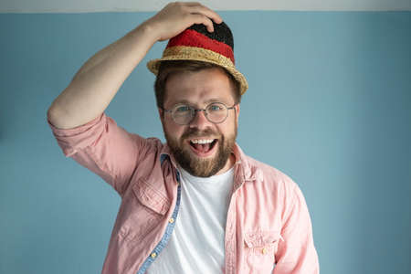 Cheerful man in a small multi-colored straw hat, raising it, greets someone and smiling joyfully....