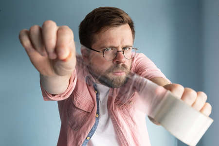 Serious man holds a roll of transparent adhesive tape in outstretched hands, he is focused and is about to pack a parcel.の写真素材