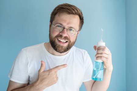 Cute smiling man holds a portable irrigator in hand, he recommends this oral hygiene product and...