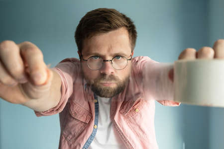 Serious man holds a roll of transparent adhesive tape in outstretched hands, he is focused and is about to pack a parcel.の写真素材