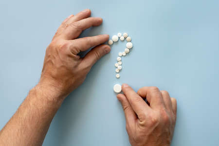 Hands folding pills in the form of a question mark. Concept of drug addiction temptation or preparation for the cold season.の写真素材