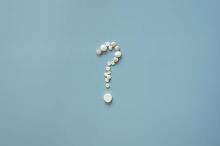 Pills are laid out in the form of a question mark, on a blue background. Medical concept or addiction to prohibited drugs. Top view.の写真素材