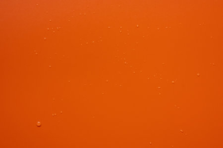 Red background with barely noticeable drops of splashed water on the surface. Copy space. Top view.