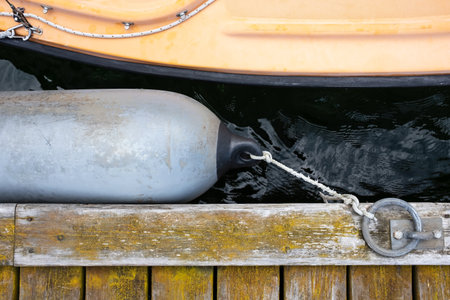 Marine fender tied with a rope to a metal ring on an old weathered pier protects the boat from damage. Top view.の写真素材