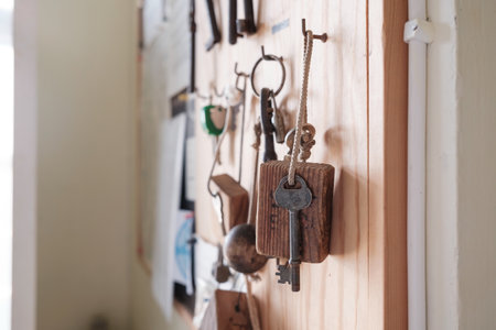 Vintage door key with a wooden keychain hangs on a hook on a board, on a blurred background.の写真素材