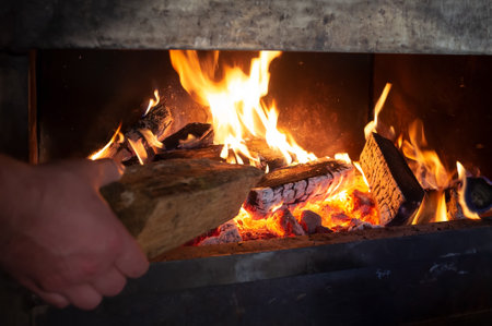 Hand puts a log on a fire to heat a homeの写真素材
