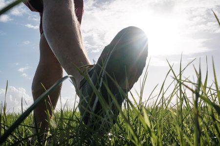 Foot in sneakers walks along a meadow, against the backdrop of the sun and sky. Active lifestyle and...