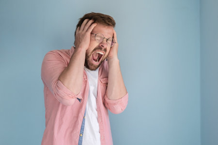 Attractive man in stress and despair, he screams loudly widely and holds head with hands. Copy space. Concept of psychological health.の写真素材