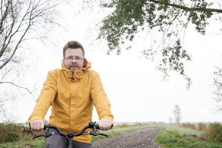 Attractive man in a yellow windbreaker on a bicycle, on a foggy morning, on a rural road with fields in the background. Lifestyle.の写真素材