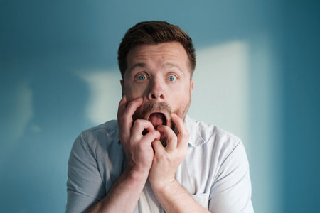 European man with a frightened, anxious expression stands against a blue background.の写真素材