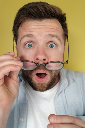 Man with a shocked expression holds his glasses, which he took off in surprise. Close-up.の写真素材