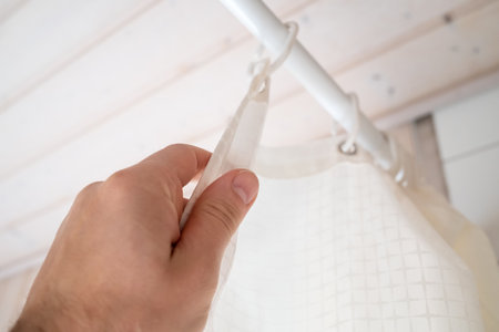 Hand closes a waterproof curtain in the bathroom, which covers the shower and prevents moisture from...