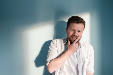 Mysterious man smiles leaning against the wall in the rays of sunlight. Copy space.