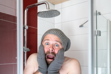 Freezing man in a hat and mittens in the shower under cold water. Concept of energy crisis.の写真素材