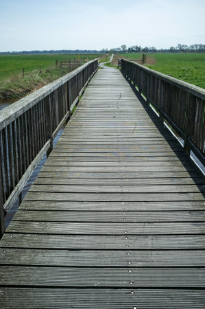 Pedestrian bridge passes over a moat filled with water, against the backdrop of fields.の写真素材