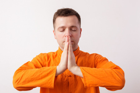 Man in an orange shirt meditating ethnicity, palms together at chestの写真素材