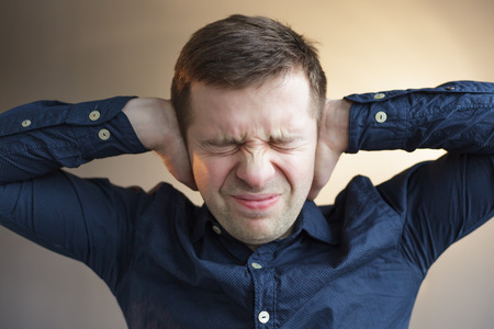man stops his ears with fingers, screaming with grief and despair. Problems at work, stress from...