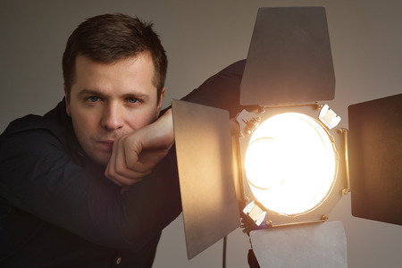 Young man stands next to the lighting equipment in the studio.