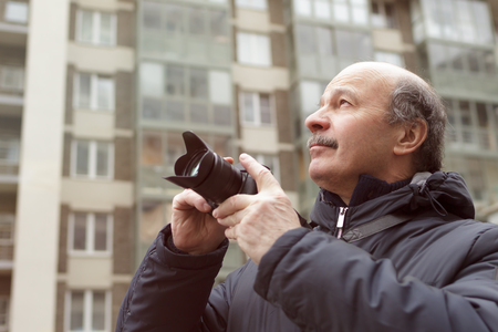 An elderly man with a mirrorless camera chooses a frame on the streetの写真素材
